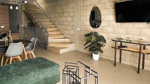 Una sala de estar moderna con una escalera, un televisor de pantalla plana, una zona de comedor y un sofá verde.