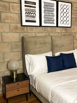 A bedroom with a bed, nightstand, lamp, and three framed artworks on the wall.