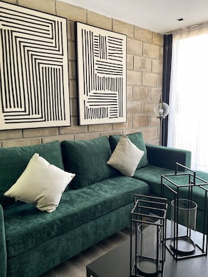 A green sofa with white cushions, a black coffee table, and two abstract wall art pieces.