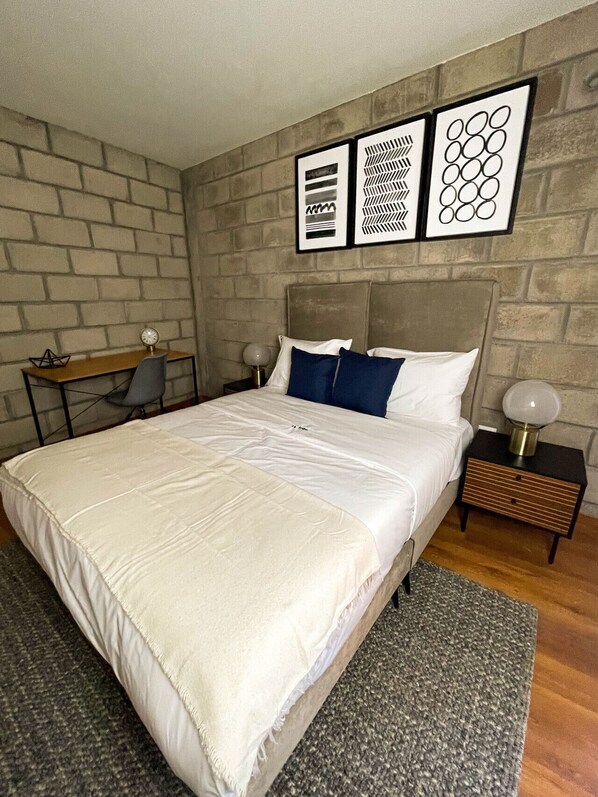 Un dormitorio con una cama, un escritorio y una silla. Hay tres cuadros en la pared.
