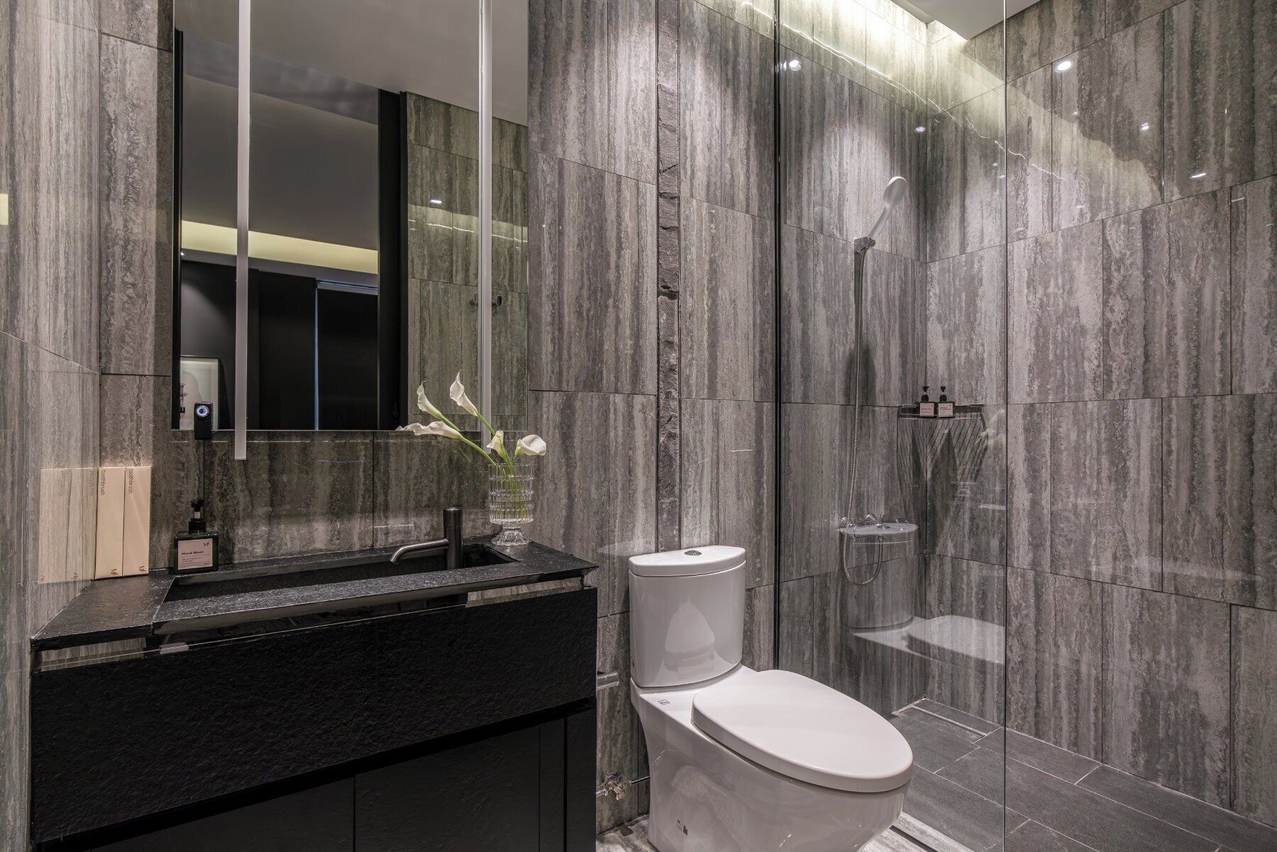 A modern bathroom with a marble wall, a black sink, a white toilet, and a glass shower enclosure.