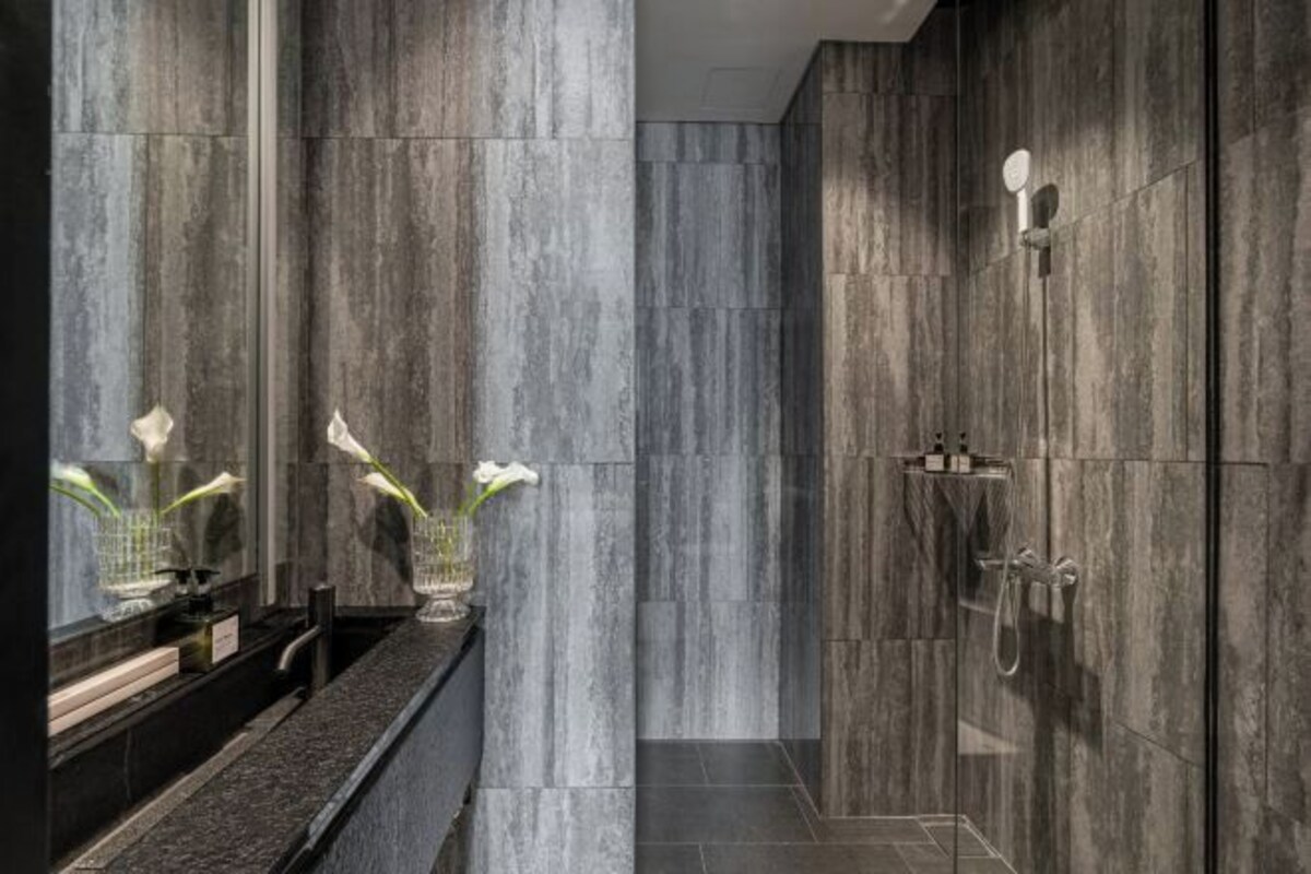 A modern bathroom with a marble wall, a glass shower enclosure, and a sink with a vase of flowers.