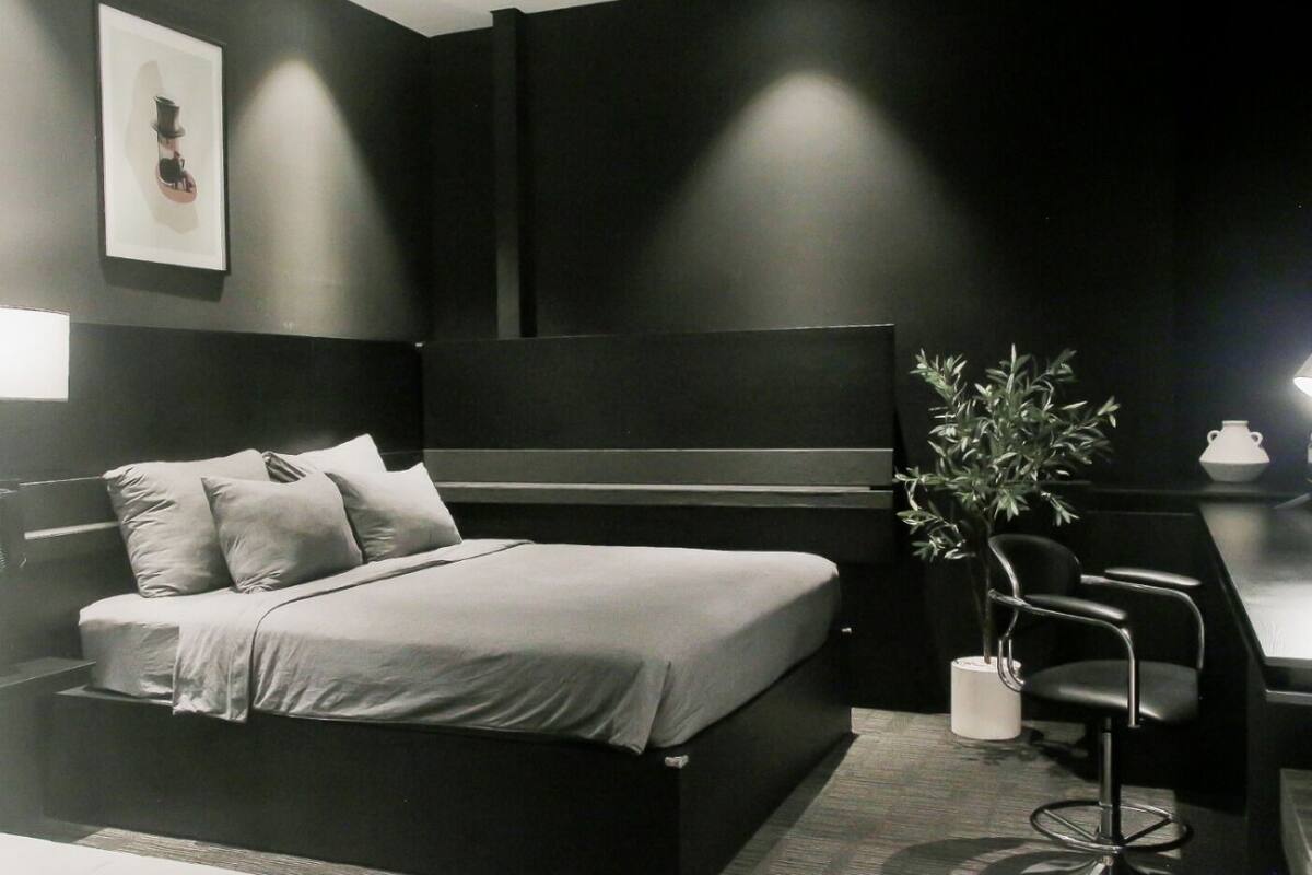 A modern bedroom with a bed, bedside table, chair, and a potted plant.