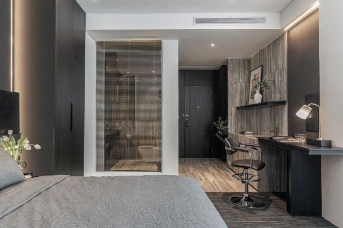 A modern bedroom with a large bed, a walk-in closet, a small kitchenette, and a seating area with a chair and table.