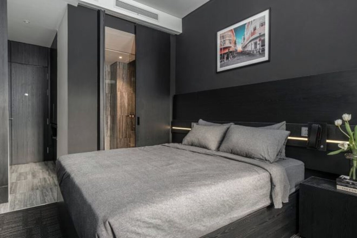 A modern bedroom with a large bed, dark walls, and a framed picture on the wall.