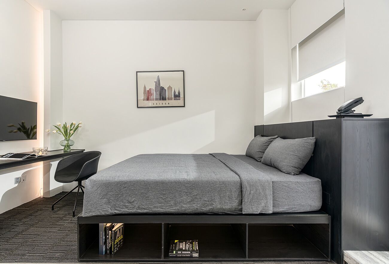 A modern bedroom with a bed, a desk, and a chair. There is a framed cityscape picture on the wall.