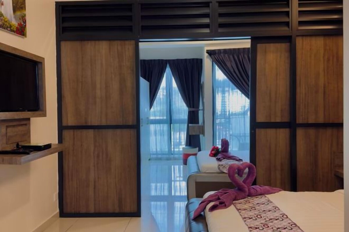 A modern hotel room with a bed, a flat-screen TV, and a view of the city through large windows.