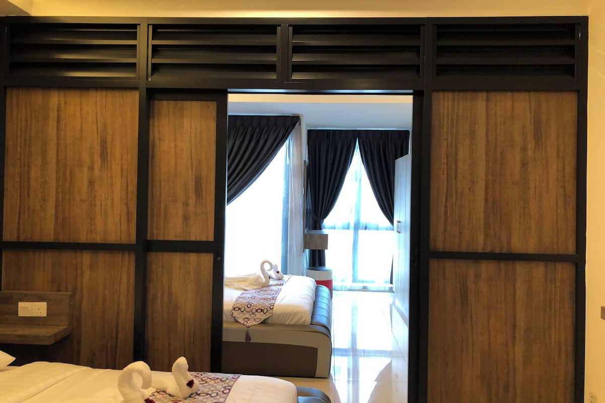 A hotel room with a wooden partition, a bed with a patterned bedspread, and a view of another room with a bed and a window.