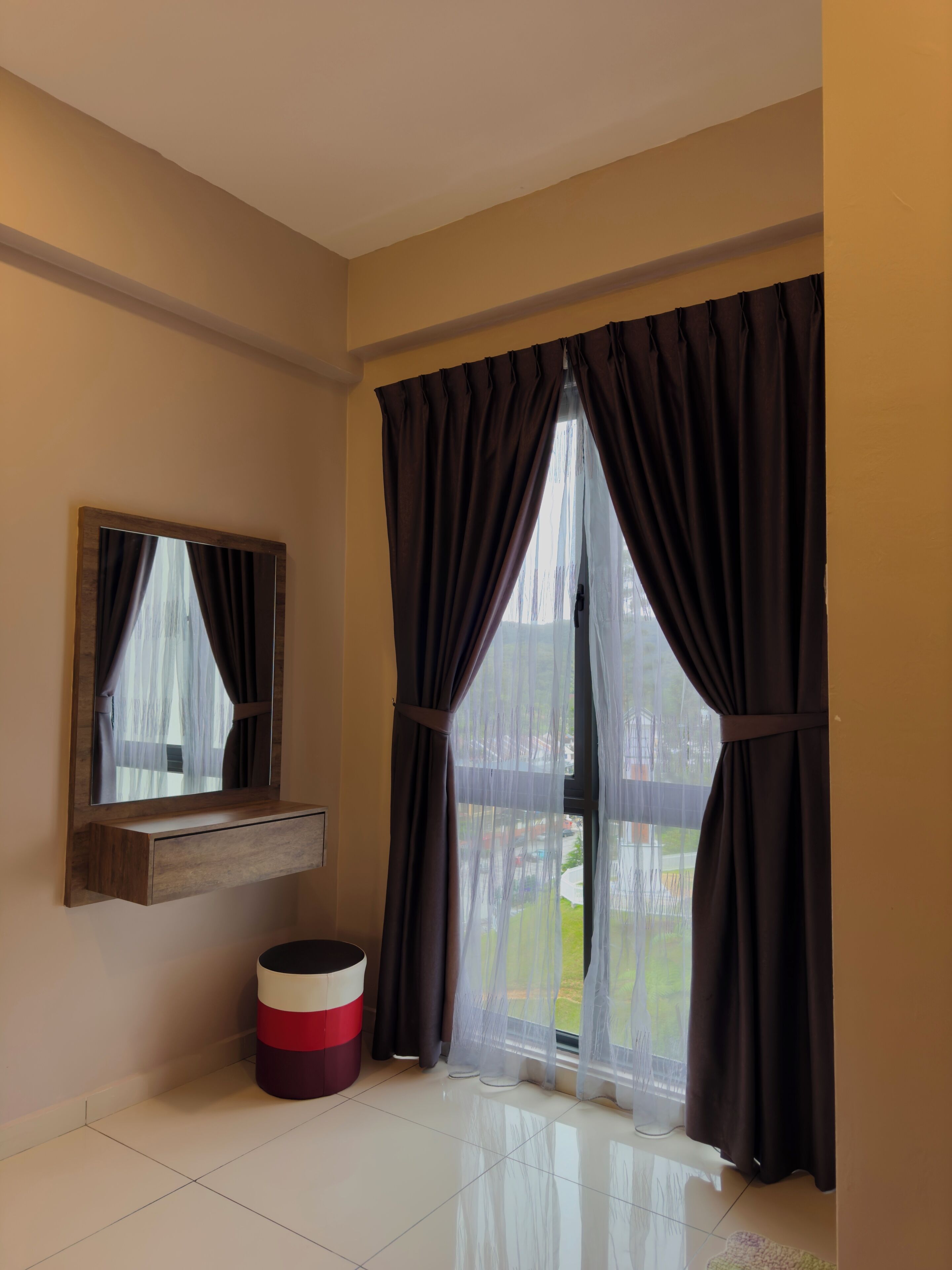 Una habitación con un ventanal grande, un espejo, un taburete pequeño y un estante fijado a la pared.