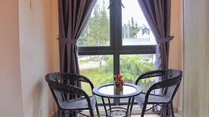 A room with a large window, two wicker chairs, and a small table with a vase of flowers.