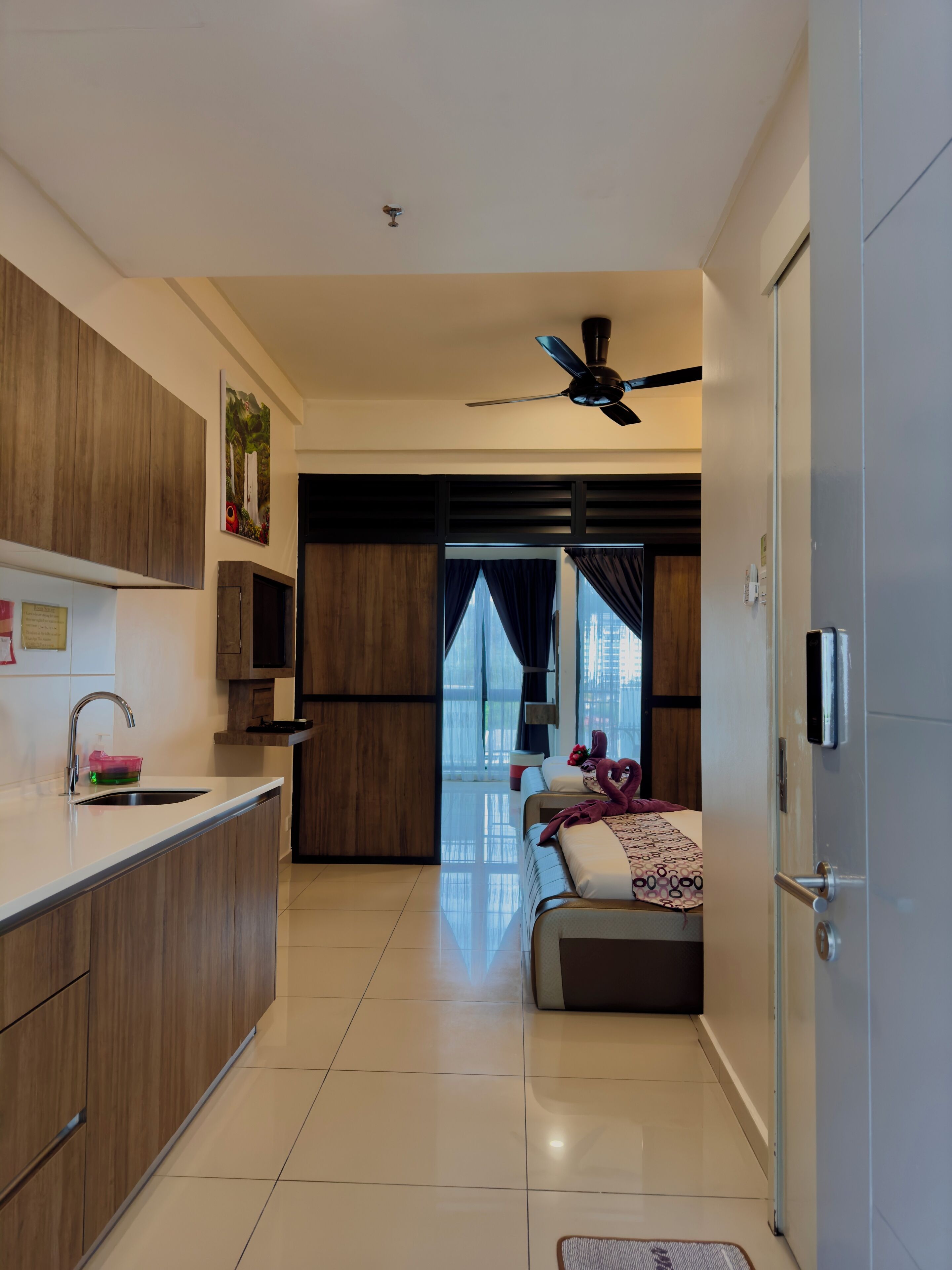 Una cocina moderna con un lavamanos integrado y armarios de madera, un comedor con sofá y alfombra decorativa, y vistas a la ciudad a través de amplios ventanales.