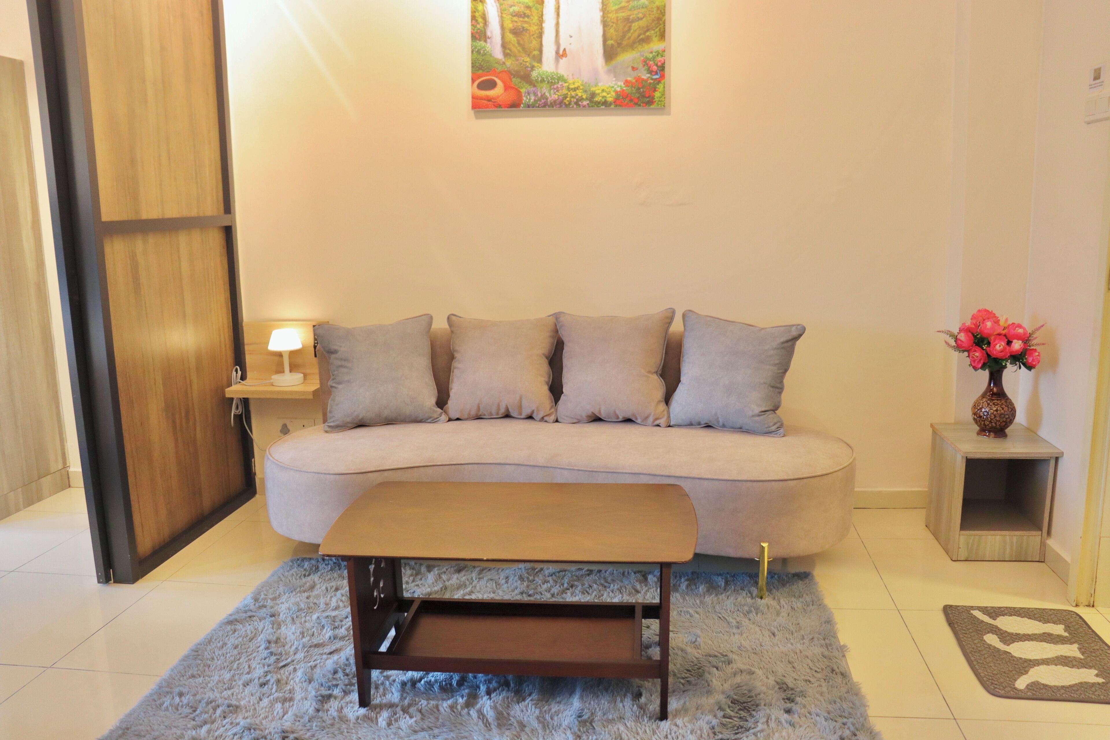 A living room with a sofa, a coffee table, a lamp, a painting, and a small side table with a vase.