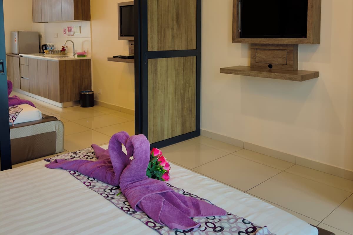 A hotel room with a bed, a TV mounted on the wall, and a painting above the TV.