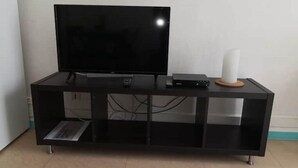 Et sort underholdningsmøbel med et fladskærms-tv, DVD-afspiller og højttaler.