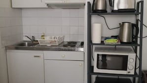 Et kompakt køkken med opvaskemaskine, mikrobølgeovn, elkedel og brødrister på en sort hylde.