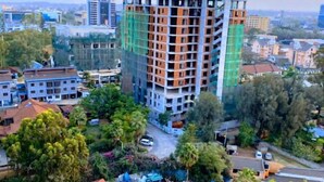 Un immeuble à plusieurs étages doté d’une architecture moderne, entouré d’arbres et d’autres immeubles résidentiels.
