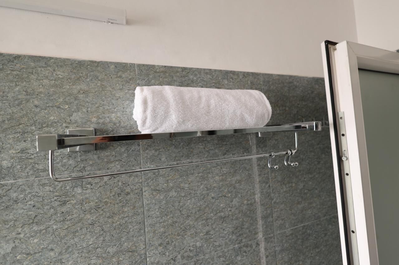 Een badkamer met een handdoekhouder met een witte handdoek, een douchegedeelte en een betegelde muur.