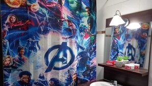 Ein Badezimmer mit einem Marvel-Duschvorhang, einem Waschbecken, einem Spiegel und einem Regal mit Pflanzen und einer Marvel-Tasse.