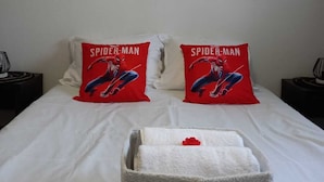 Ein Hotelzimmer mit einem Bett, zwei Spider-Man Kissen, einer weißen Decke und Wandkunst mit verschiedenen Superhelden.
