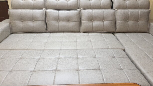 A sectional sofa with a tufted design and wooden legs. - Private Flat with open space WiFi and AC in charming Varanasi near Assi Ghat (Varanasi)