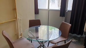 A small meeting room with a glass table and four chairs, a window with curtains, and a yellow wall. - Private Flat with open space WiFi and AC in charming Varanasi near Assi Ghat (Varanasi)