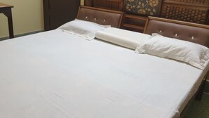 A neatly made bed with white linens in a room with a wooden headboard and a small table with a chair. - Private Flat with open space WiFi and AC in charming Varanasi near Assi Ghat (Varanasi)