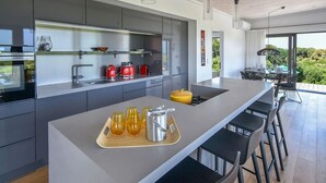 A modern kitchen with a central island, grey cabinetry, and a dining area with black chairs.