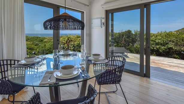 A modern dining area with a glass table and black wicker chairs, overlooking a scenic landscape.
