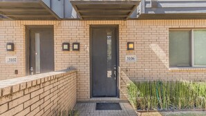 A modern building with two numbered doors, 3102 and 3106, and a small entrance area with a brick wall and a narrow pathway. - Modern 2 BR, 4 Story Smarthome with Rooftop Hot Tub, Game Room and Skyline Views (Dallas)