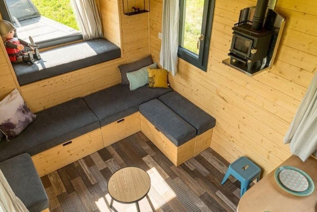 L’intérieur d’un chalet accueillant, avec un canapé intégré, une petite table ronde, un tabouret bleu et un poêle à bois.