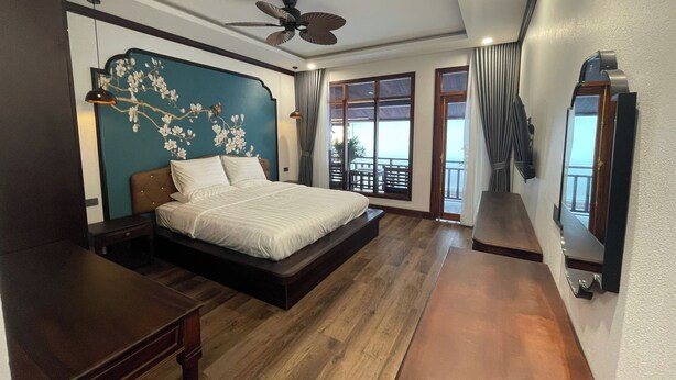 A bedroom with a bed, a ceiling fan, a large window, and a view of the outside.