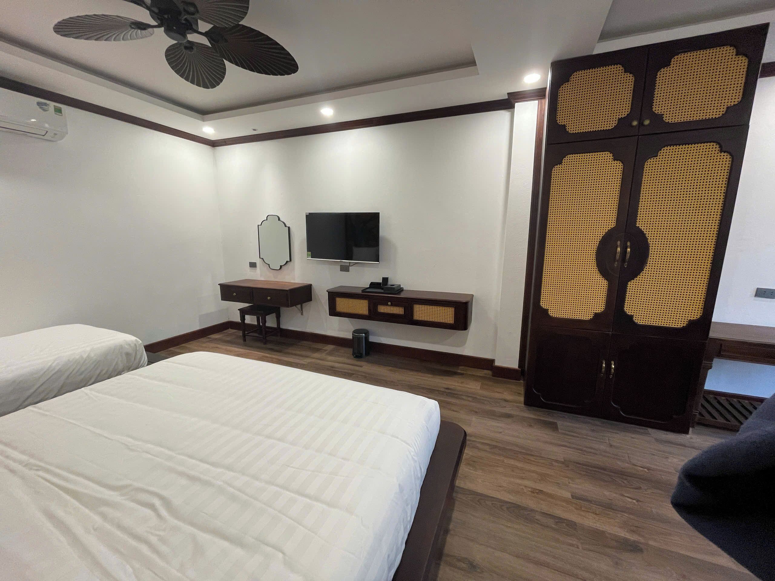 A hotel room with two beds, a desk with a television, a mirror, and a traditional door.
