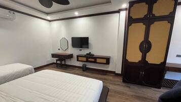 A hotel room with two beds, a desk with a television, a mirror, and a traditional door.