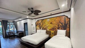 A hotel room with two beds, a ceiling fan, an air conditioning unit, and a large autumn-themed mural on the wall.