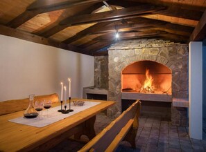 Una chimenea de piedra con fuego, vigas de madera, una mesa con velas y un banco.