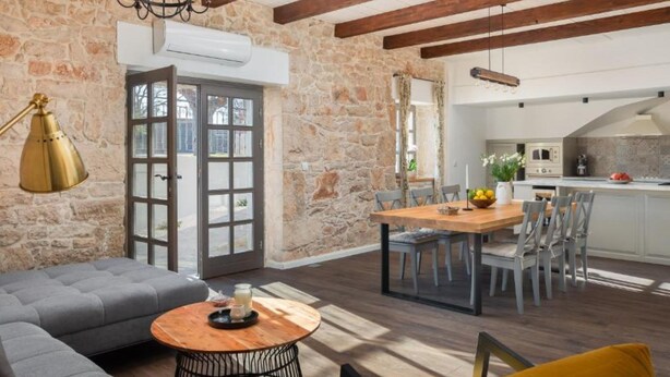 A spacious living area with a stone wall, a wooden ceiling, a dining table with chairs, and a sofa. - Villa Casa Di Pietra (Sibenik)