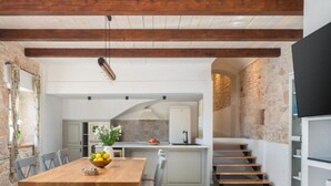 A spacious kitchen with a wooden dining table, a built-in island, and a staircase leading to an upper level. - Villa Casa Di Pietra (Sibenik)