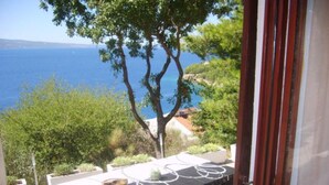 A terrace with a table set for dining, overlooking a scenic view of the sea and greenery. - Apartments Roma (Omis)