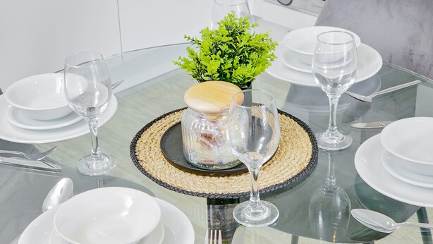 A dining table set with white plates, bowls, cutlery, and wine glasses, centered around a decorative centerpiece with a small plant and a glass jar. - Salford - 2 Bed Apartment - Sleeps 4 - Wifi (Salford)