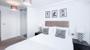 A modern bedroom with a large bed, two bedside tables with lamps, a headboard, and three framed pictures on the wall. - Salford - 2 Bed Apartment - Sleeps 4 - Wifi (Salford)