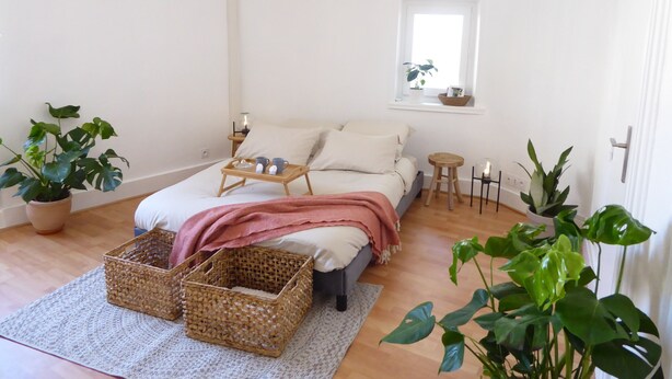 Un dormitorio con cama, mesitas de noche, una ventana y plantas en macetas.