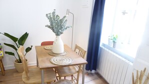 Una mesa de comedor de madera con individuales tejidos, rodeada de sillas de madera. Un jarrón blanco con follaje verde está sobre la mesa.