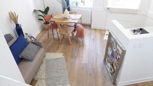 Una sala de estar moderna con un sofá, una mesa de comedor con sillas, una zona de cocina con un lavamanos y una ventana con plantas.