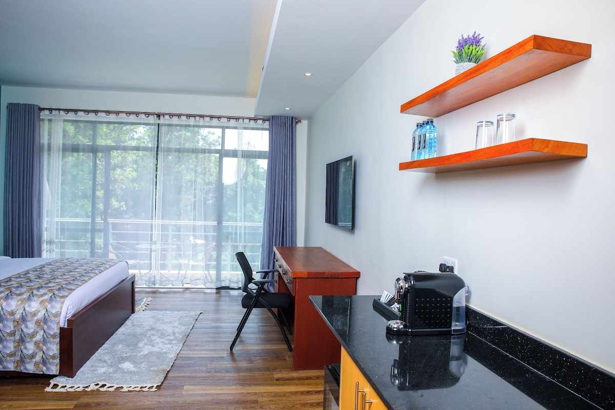 Une chambre avec un lit, un bureau et une machine à café. Il y a une fenêtre avec des rideaux, une chaise et une plante sur une étagère.