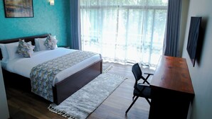 A hotel room with a bed, a desk, a chair, a large window with curtains, and a painting on the wall. - Hidden Hills Luxury Boutique Hotel (Nairobi)
