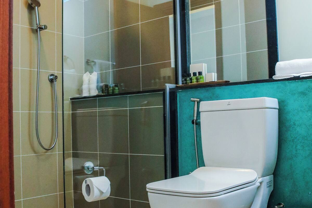 Un baño moderno con ducha envuelta en vidrio, inodoro blanco y un cubo de basura.