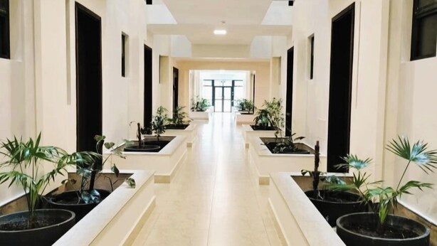 A long, narrow hallway with a tiled floor, flanked by white walls and black-framed windows. There are potted plants placed at regular intervals along the hallway. - Hidden Hills Luxury Boutique Hotel (Nairobi)