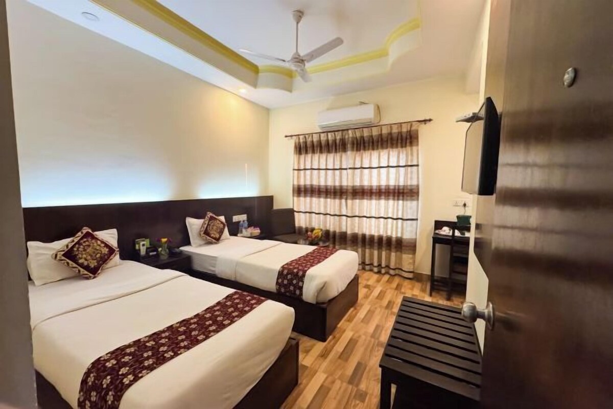 A hotel room with two beds, a ceiling fan, an air conditioning unit, a desk, and a window with curtains.