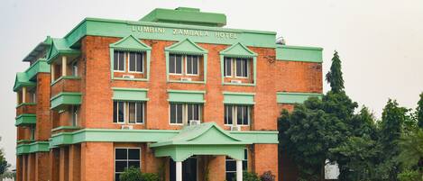 Un gran edificio de ladrillo con techo verde y columnas, con la leyenda "LUMBINI ZAMBALA HOTEL".