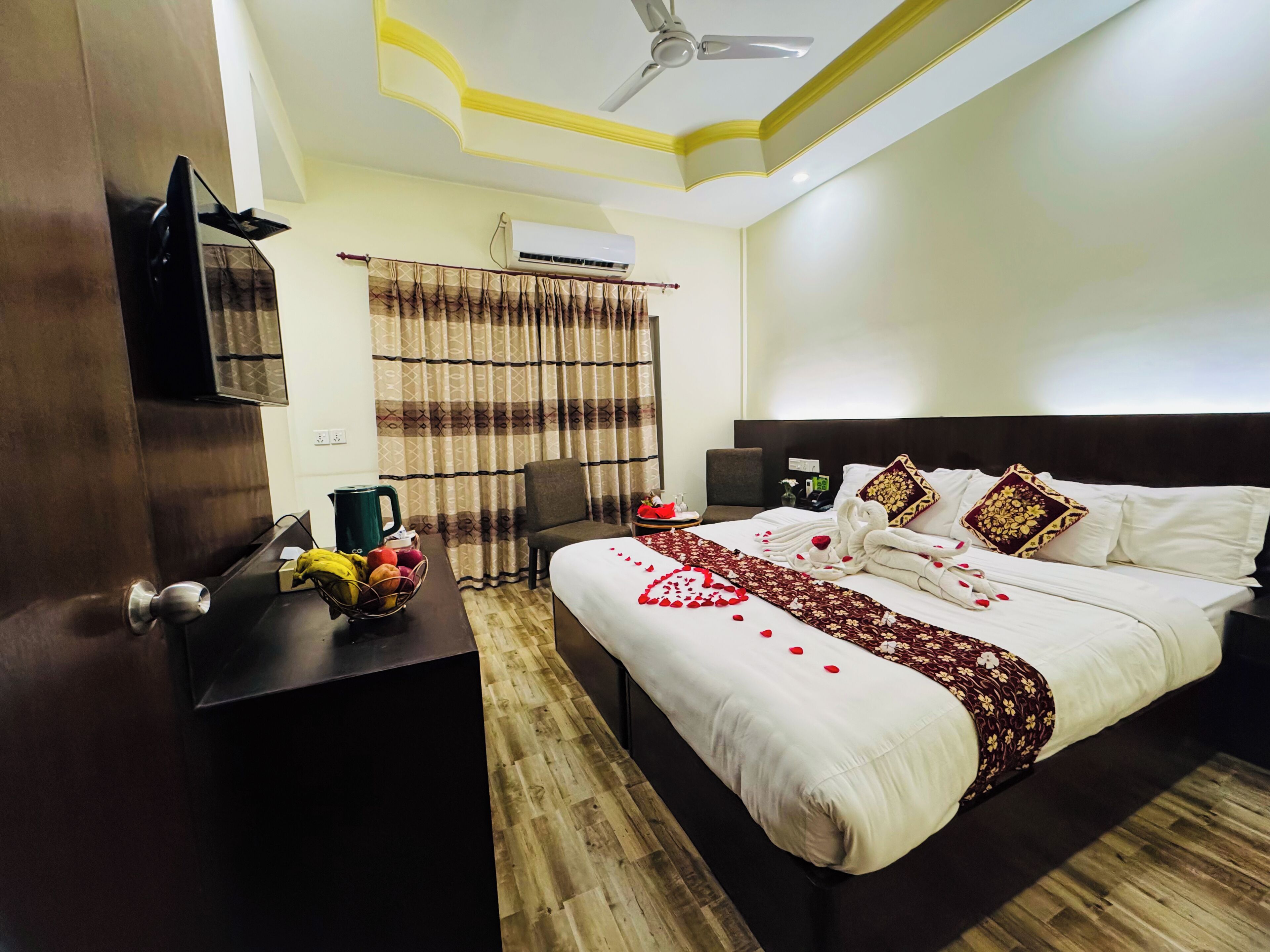 A hotel room with a bed, a desk, a chair, a ceiling fan, an air conditioning unit, and a window with curtains.